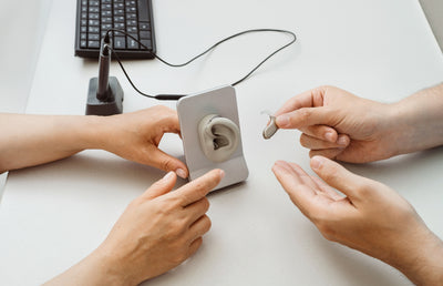 Two people putting a hearing aid on a model of an ear.