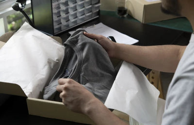 Someone packing a t shirt into a box for shipping.