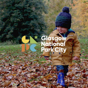 A child playing in leaves with the Glasgow National Park City logo.